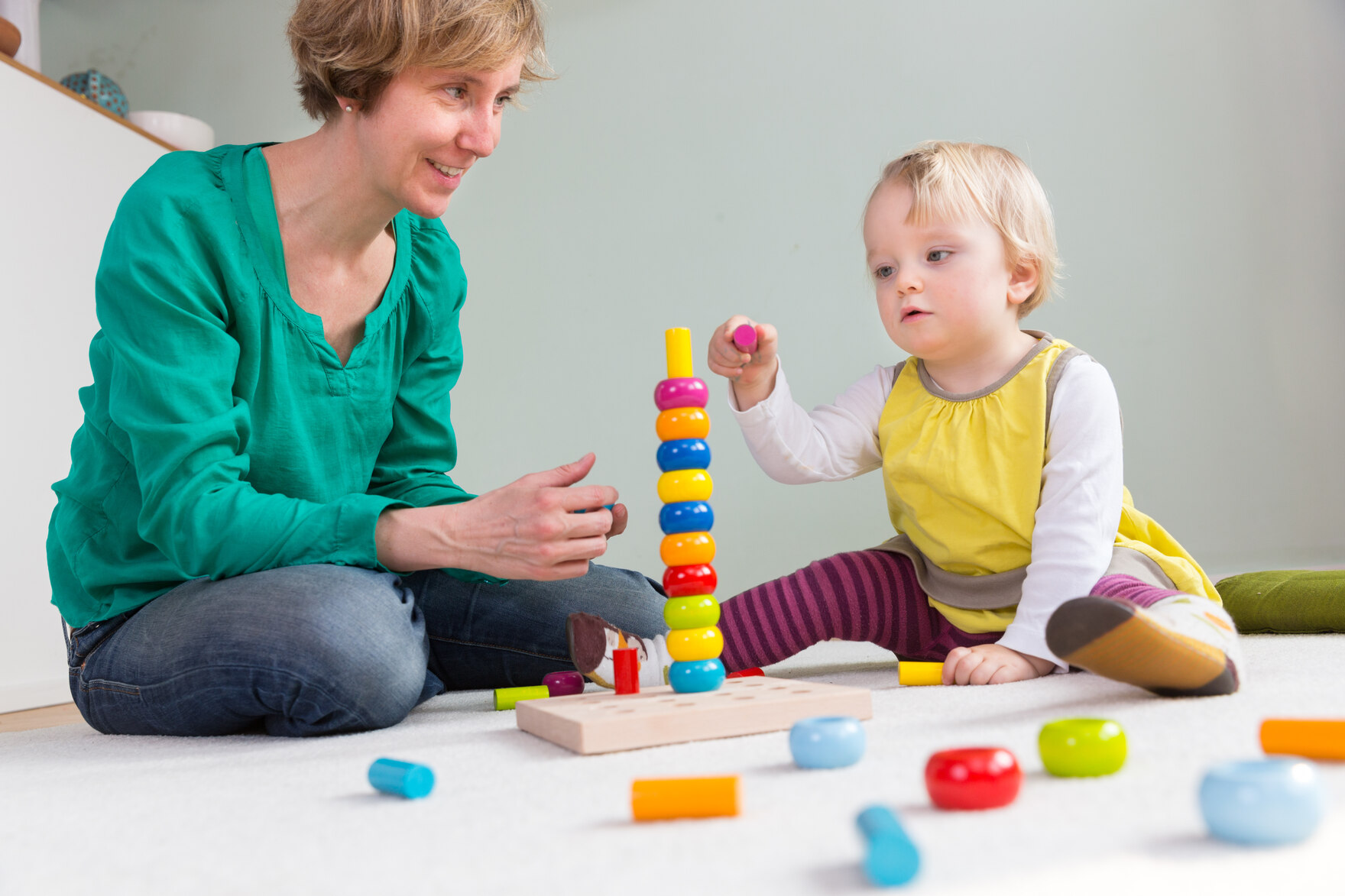 Eine Tagesmutter spielt mit einem kleinen Mädchen auf dem Boden