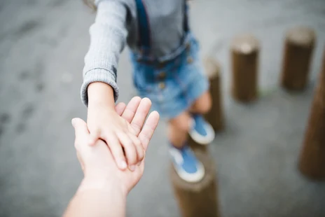 ein keines Kind greift Hilfe suchend nach der Hand eines Erwachsenen