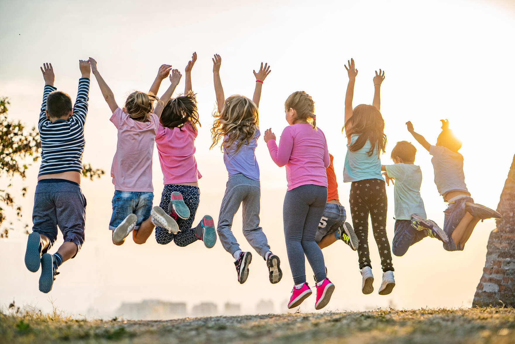 eine Gruppe mehrerer Kinder von hinten zu sehen springt jubelnd in die Luft