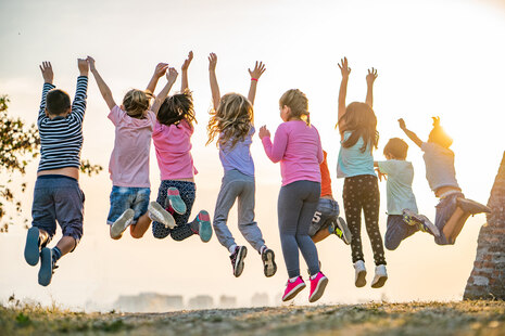 mehrere Kinder von hinten zu sehen, springen jubelnd in die Höhr