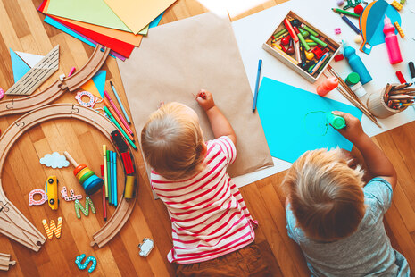 zwei Kinder liegen auf dem Laminat zwischen Spielzeug und malen