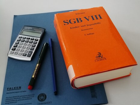 Buch SGB VIII liegt auf Schreibtisch neben Taschenrechner und Bleistift