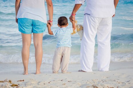 Mutter und Vater haben ihr Kind an der Hand und stehen am Strand